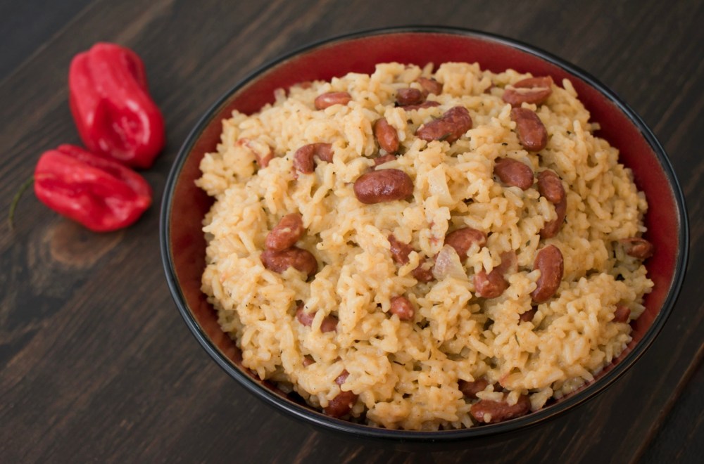 Bowl of rice and beans on a wooden surface with two red peppers beside it.