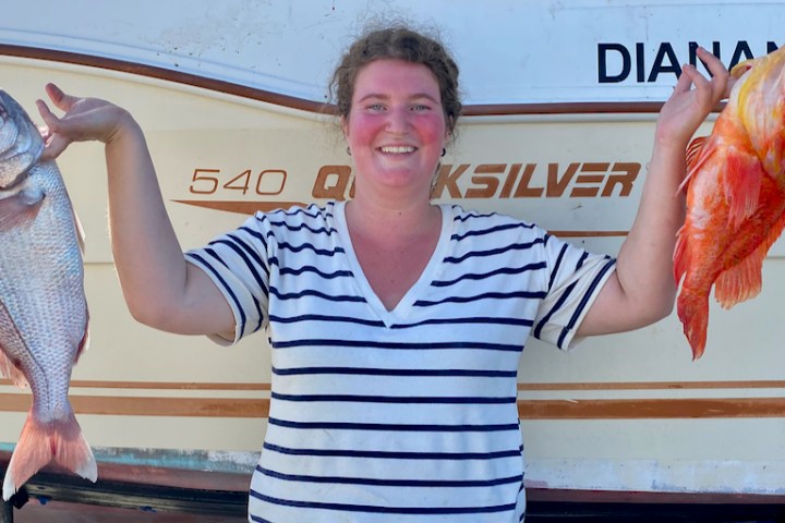a woman holding a fish on a boat posing for the camera