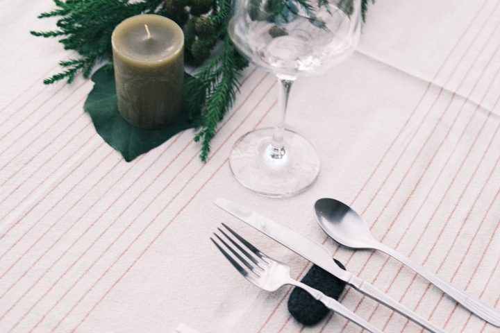 Table setting with glass, cutlery, green candle, pine decor, and a rock-name placeholder on a napkin.