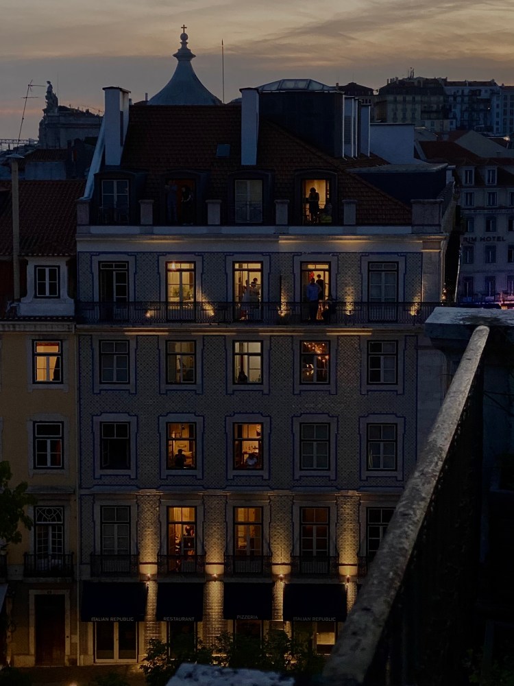Lit windows of a multi-story building at dusk with silhouetted figures visible inside.