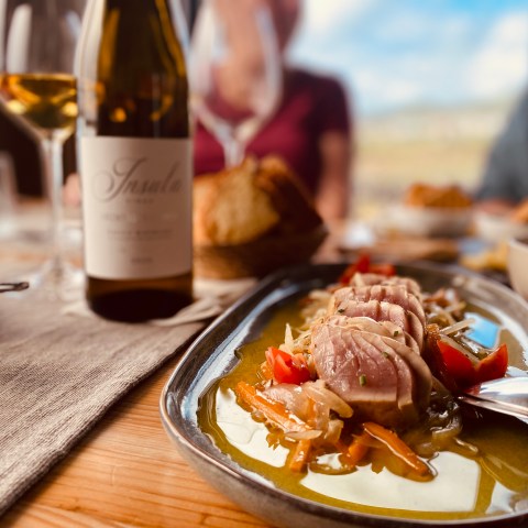Plated seared tuna with wine bottle and glasses on a rustic wooden table.