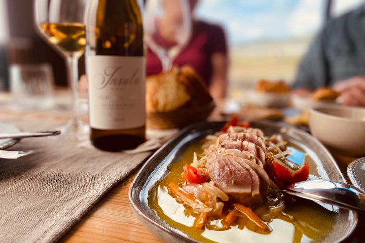 Plated seared tuna with wine bottle and glasses on a rustic wooden table.