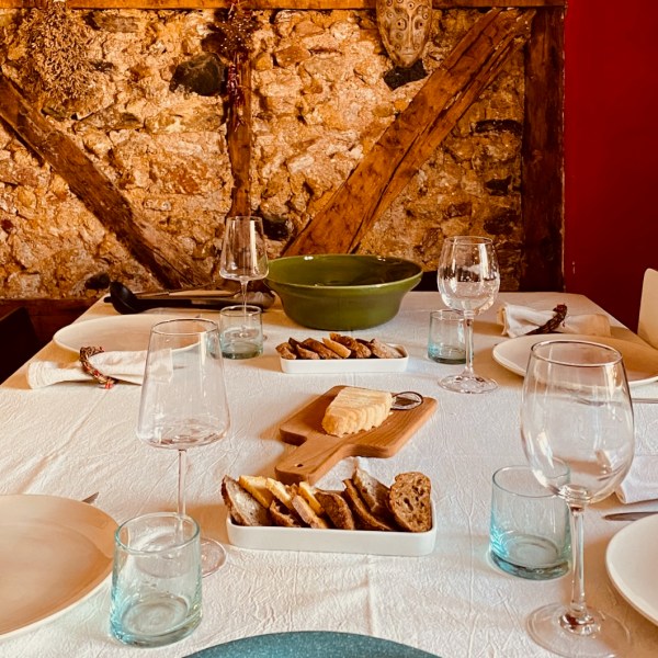 Rustic dining table with bread, cheese, and wine glasses on a white tablecloth.