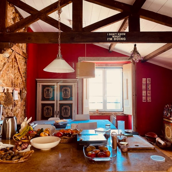 Rustic kitchen with wooden beams, red walls, and a countertop with fruits and kitchen items.