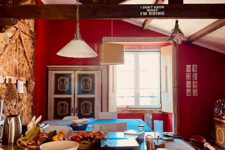 Rustic kitchen with wooden beams, red walls, and a countertop with fruits and kitchen items.