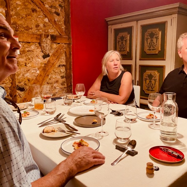 Three people seated at a dining table with plates and wine glasses, in a rustic room with exposed brick.