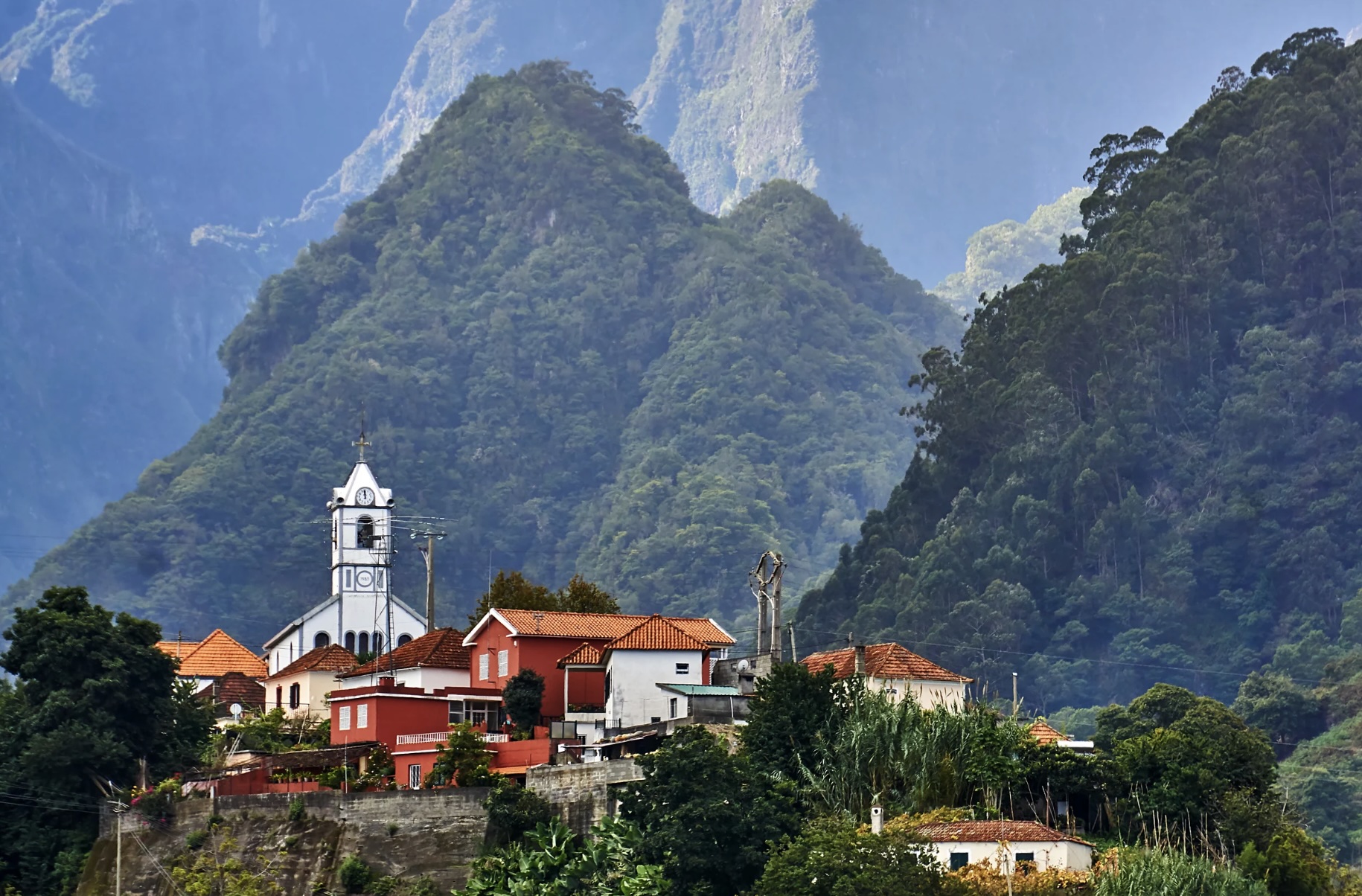 Village with red-roofed houses and church set against lush, forested mountains.