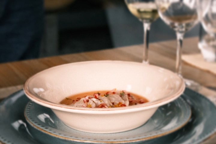 Dish of seafood soup on stacked plates with wine glasses in the background.