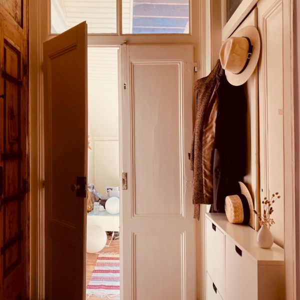 Open door to a room with hats on hooks, a cabinet, and a colorful rug on wooden floor.