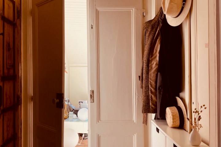 Open door to a room with hats on hooks, a cabinet, and a colorful rug on wooden floor.
