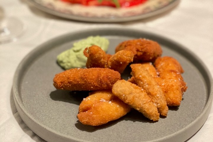 Plate of fried food with green dip in foreground, salad with cheese in background on a white tablecloth.