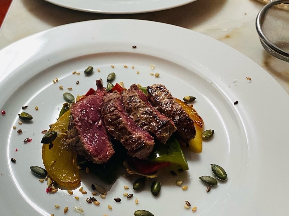 Two white plates with sliced steak on vegetables, garnished with seeds.