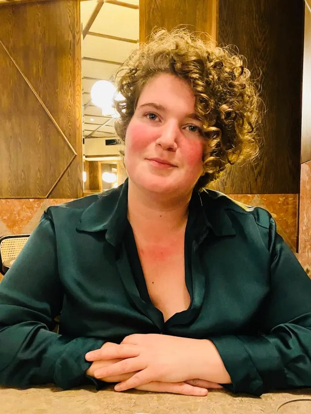 Person with curly hair in green shirt sitting at a table in a warmly lit room.
