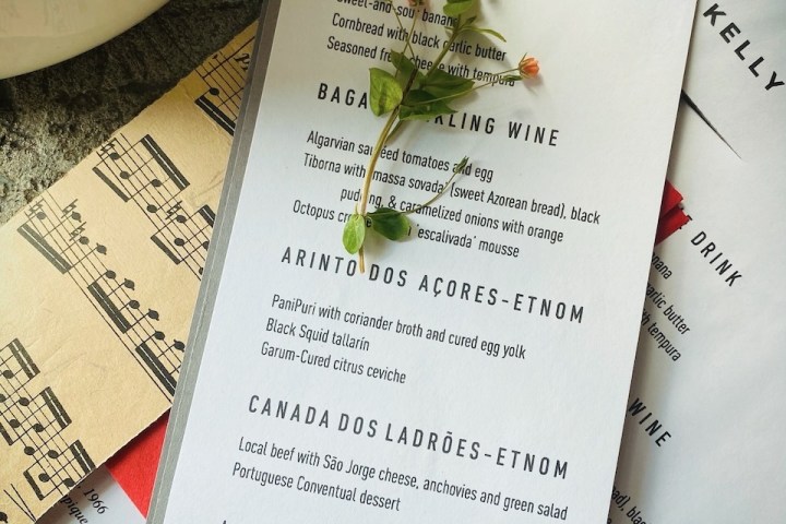 Wedding menu with wax seal and greenery on textured surface; musical sheet partially visible.