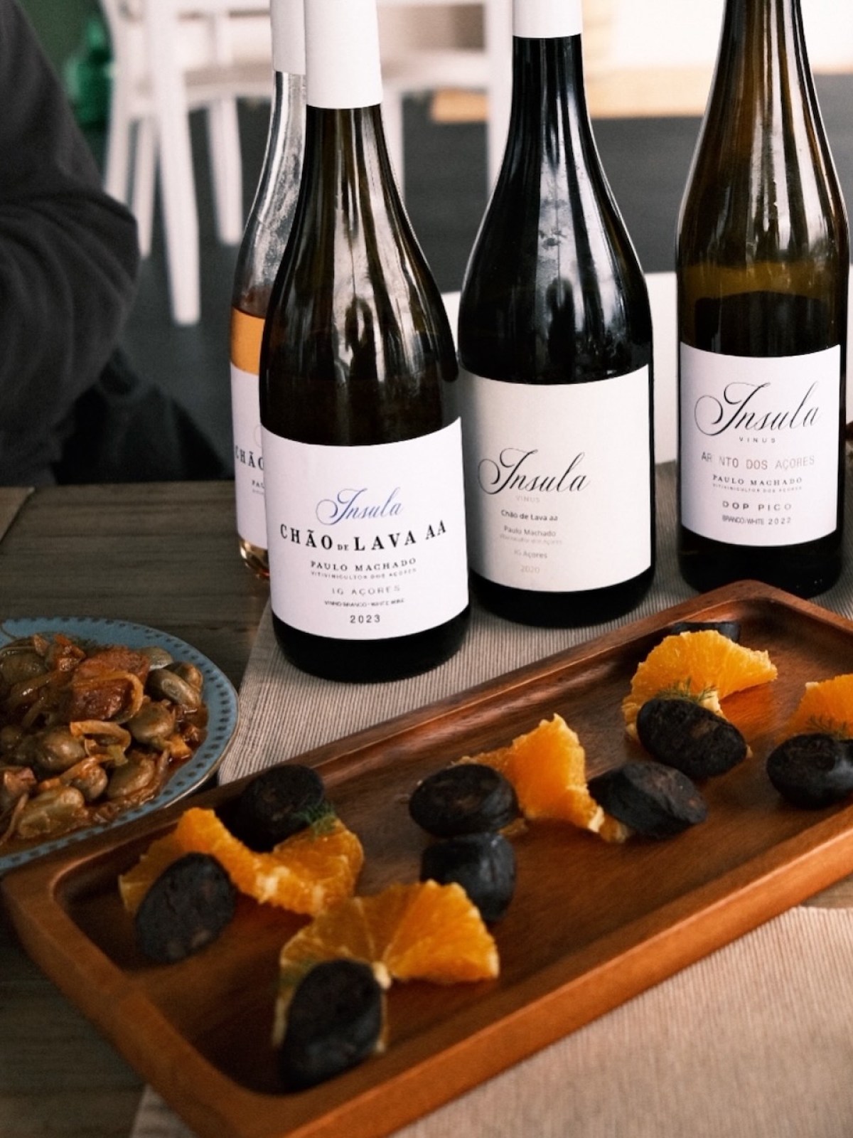 Three wine bottles, sausage, and orange slices on a wooden tray.