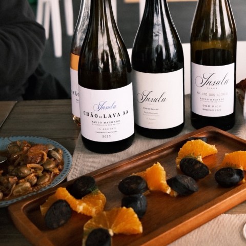Three wine bottles, sausage, and orange slices on a wooden tray.