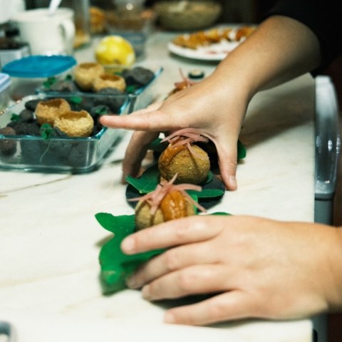 Hands preparing food on leaves, with ingredients on a kitchen counter.
