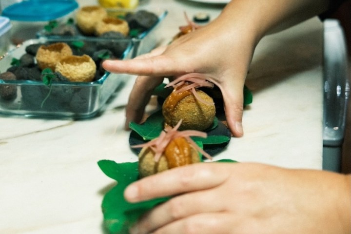 Hands preparing food on leaves, with ingredients on a kitchen counter.