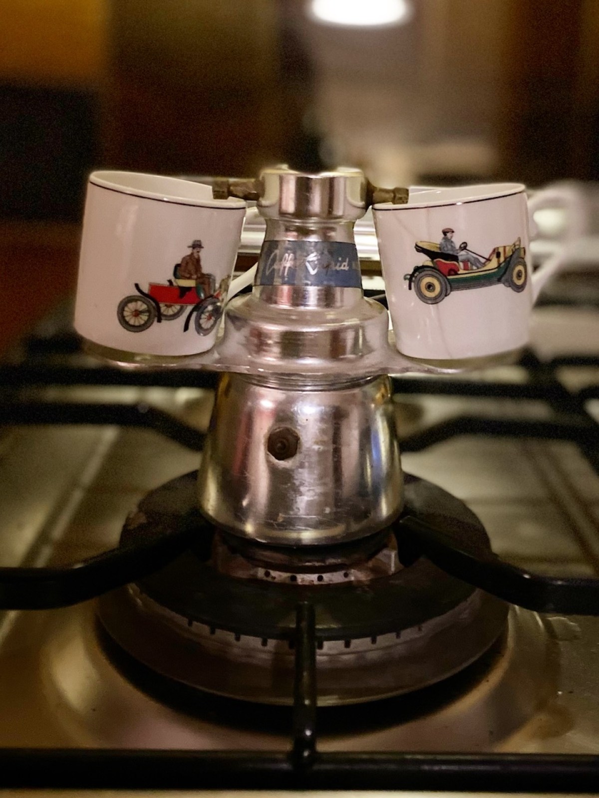 Two espresso cups on a stovetop espresso maker on a gas burner.