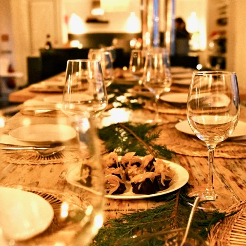 A set dining table with wine glasses, plates, and a centerpiece of greenery and small appetizers.