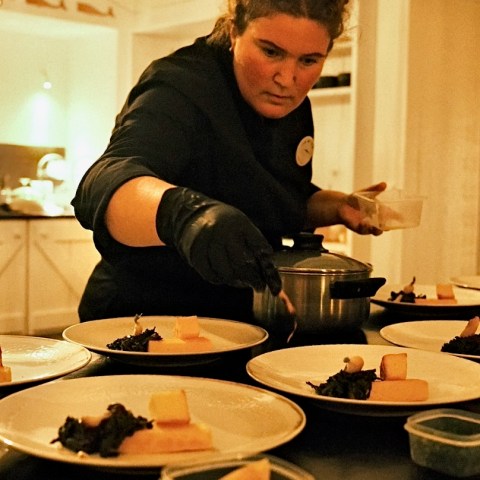 Chef plating gourmet dishes in a kitchen, focused and wearing gloves.