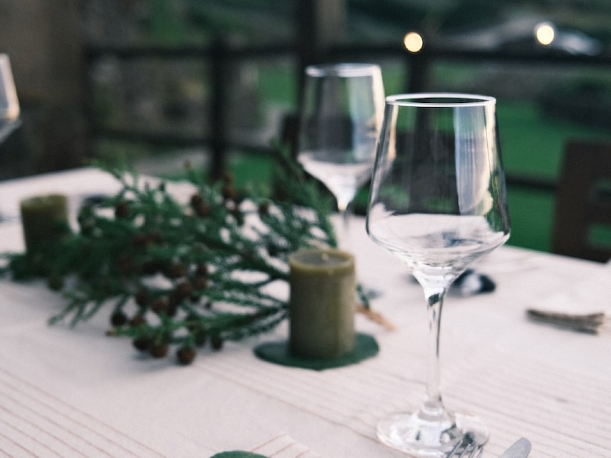 Outdoor table setting with wine glasses, utensils, candles, and foliage decoration.