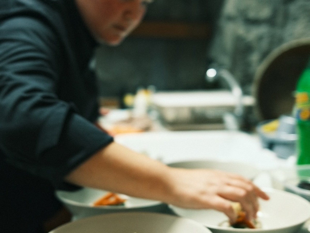 Person plating food in a kitchen, focusing on placing ingredients in bowls.