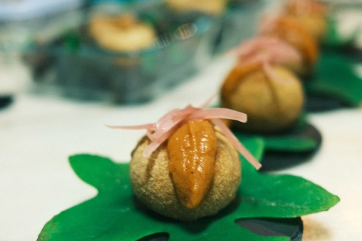 Round pastries with topping on green leaf plates on a marble surface.