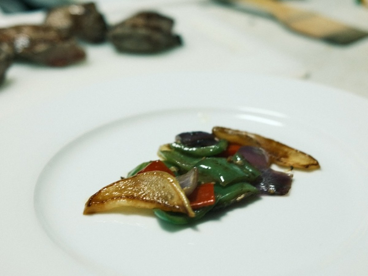Colorful stir-fried vegetables on a white plate, blurred kitchen background.