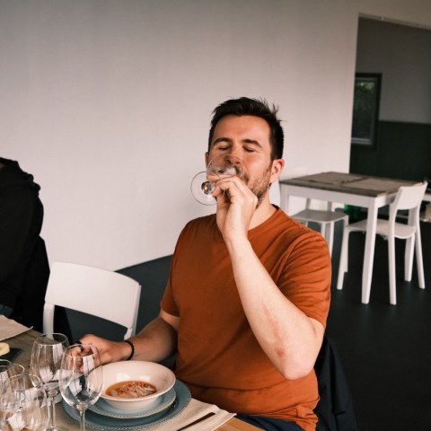 Person in an orange shirt sitting at a table drinking from a glass.