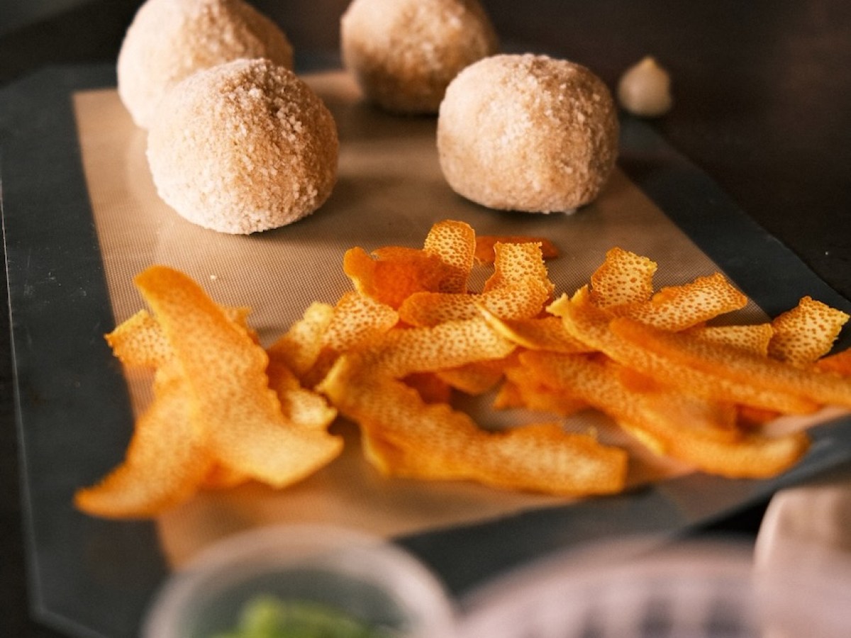 Four dough balls and orange peels on a baking sheet.