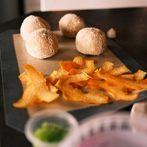 Four dough balls and orange peels on a baking sheet.