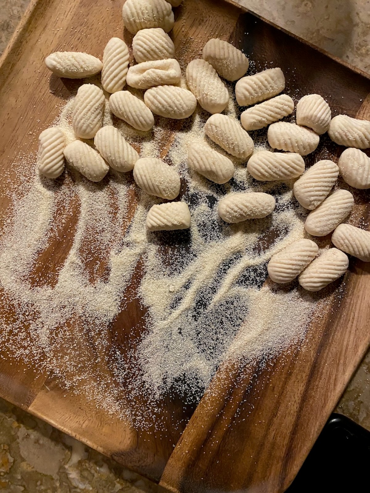 Uncooked gnocchi on a wooden board, dusted with semolina flour.