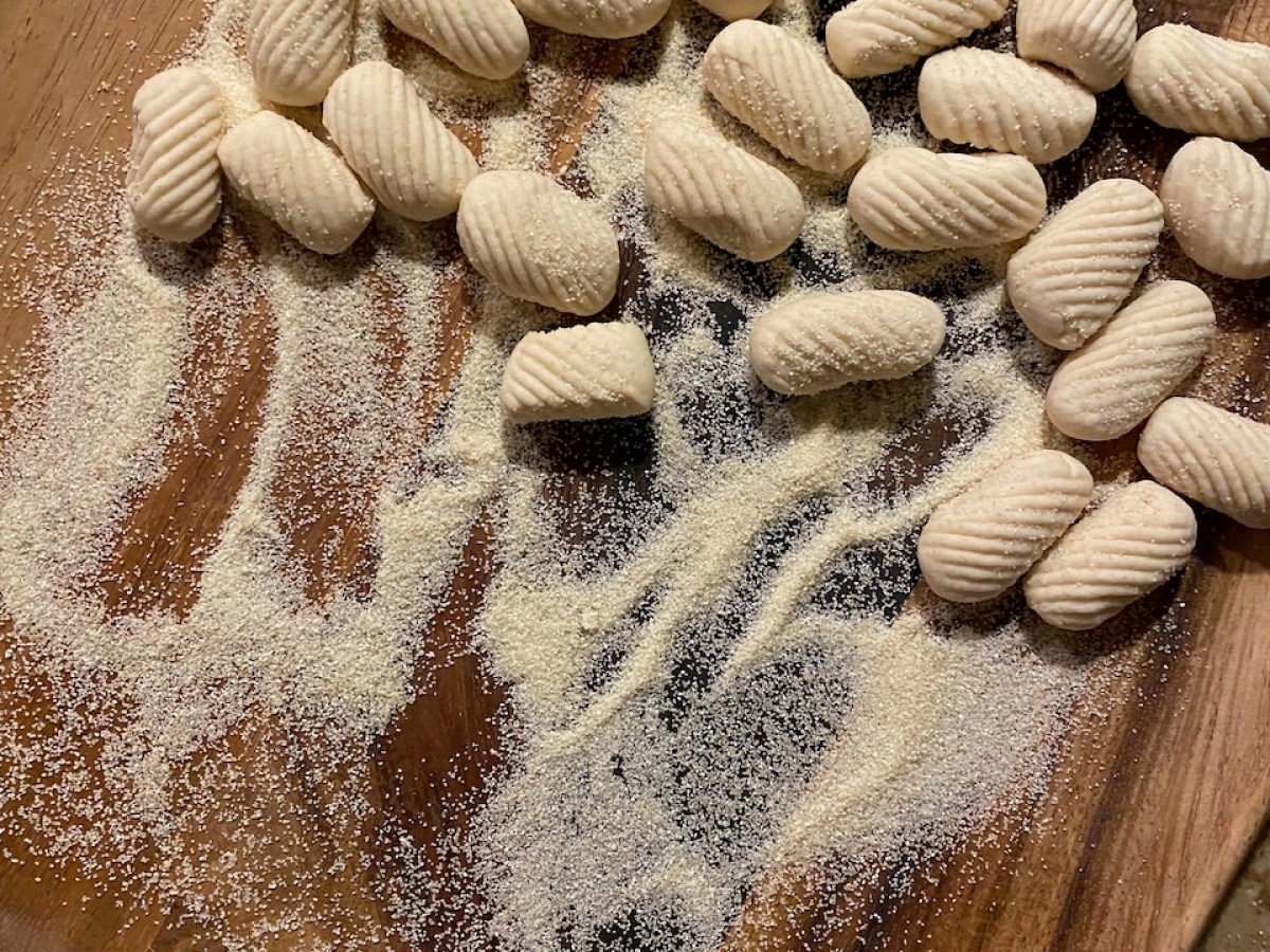 Uncooked gnocchi on a wooden board, dusted with semolina flour.