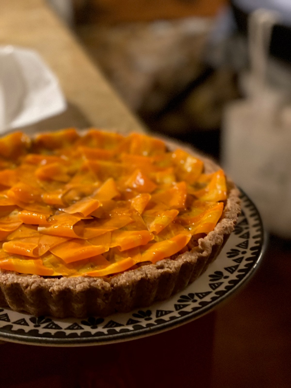 A tart with sliced orange fruit on a patterned plate, on a kitchen counter.