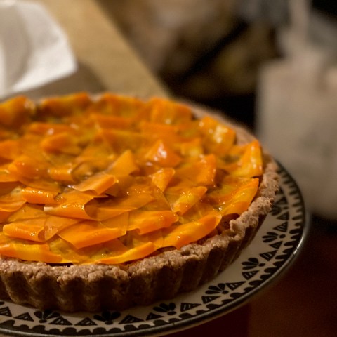 A tart with sliced orange fruit on a patterned plate, on a kitchen counter.