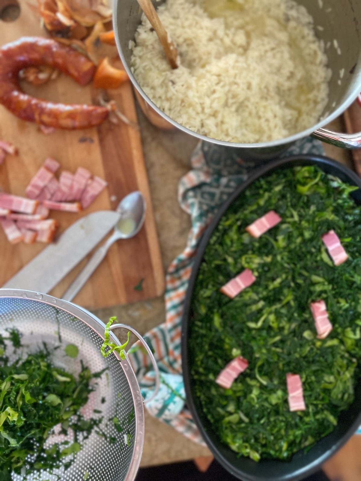 Cooking scene with rice, chopped greens, and sliced sausage on a kitchen counter.