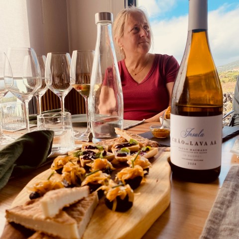 Woman in red shirt seated at table with wine, glasses, and appetizers on a wooden board.