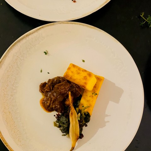 Gourmet dish with meat, polenta, and greens on a white plate.