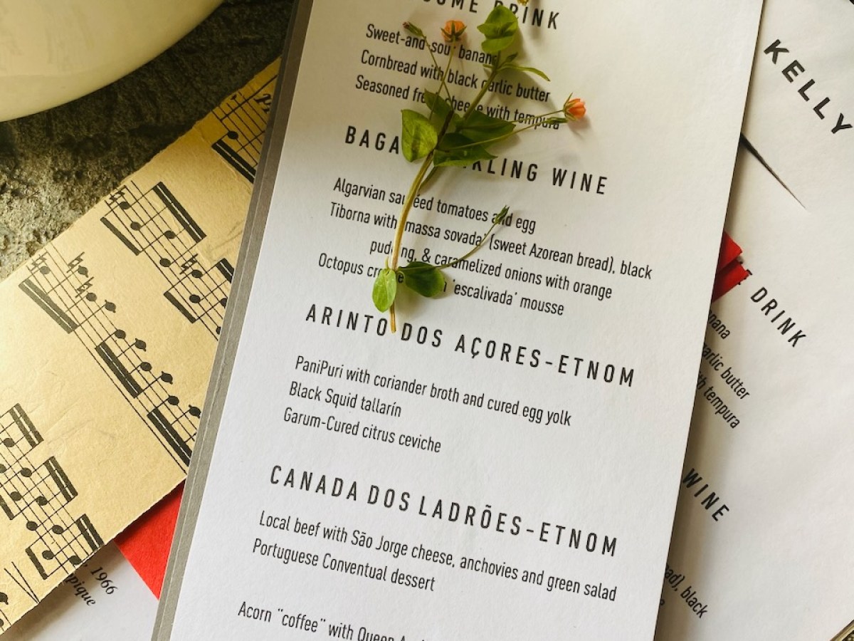 Elopement menu with a wax seal and decorative plant, placed on textured surface and sheet music.