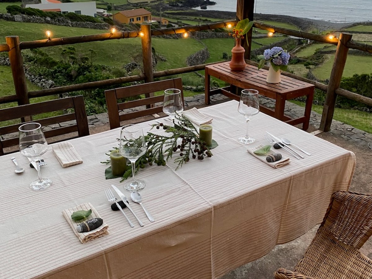 Outdoor dining table with glasses and decor, overlooking a coastline under a cloudy sky.