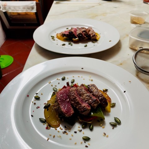 Two plates of sliced steak on a salad with seeds on a marble countertop.