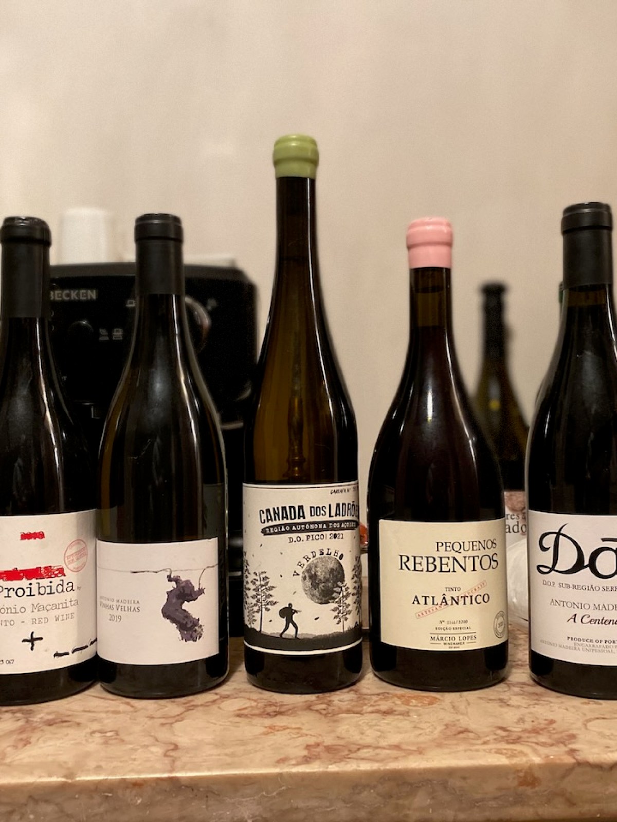 Seven wine bottles with different labels lined up on a marble countertop.