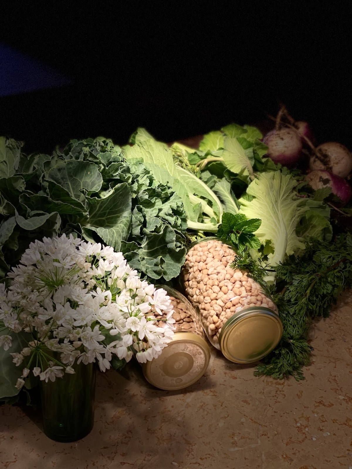 Jars of nuts, leafy greens, white flowers, and turnips on a surface.