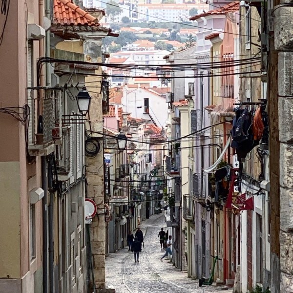 Narrow cobblestone street with colorful buildings and people walking.