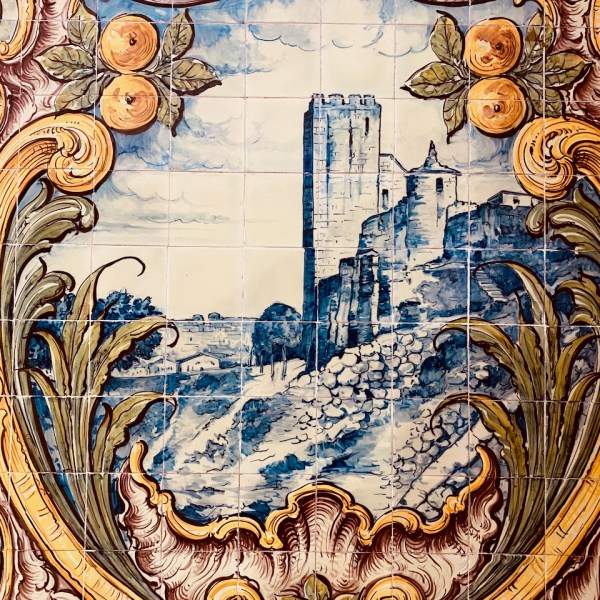 Decorative tile mural with a castle scene, surrounded by ornate floral and fruit motifs.