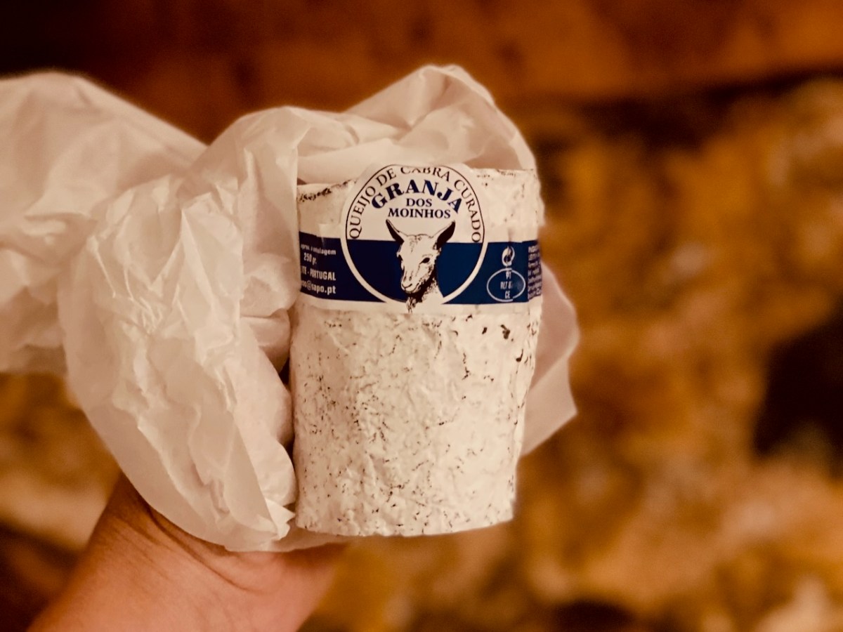 Hand holding a cylindrical package of goat cheese wrapped in white paper.