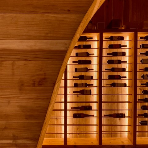 Warmly lit wooden wine cellar with bottles displayed on horizontal racks.
