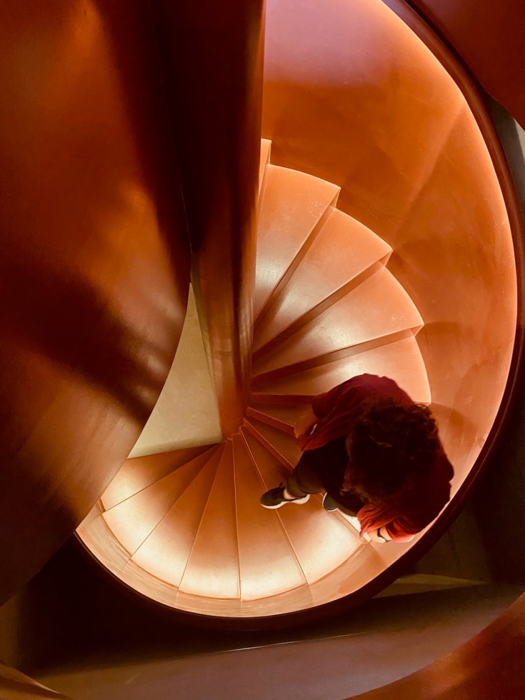 Top view of a person walking down a red spiral staircase.