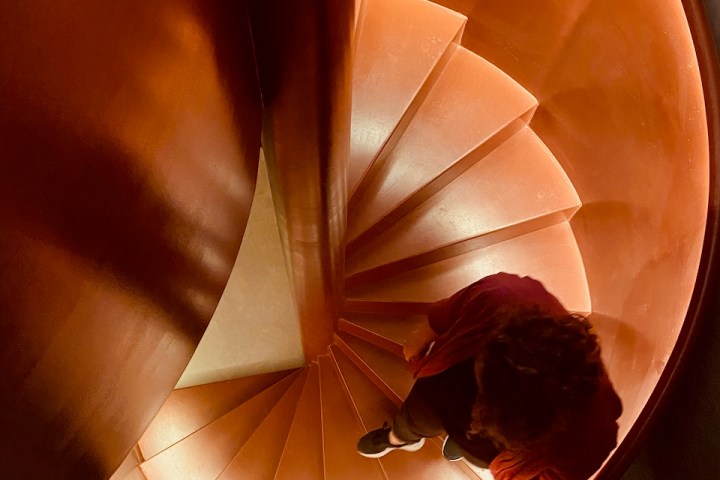 Top view of a person walking down a red spiral staircase.